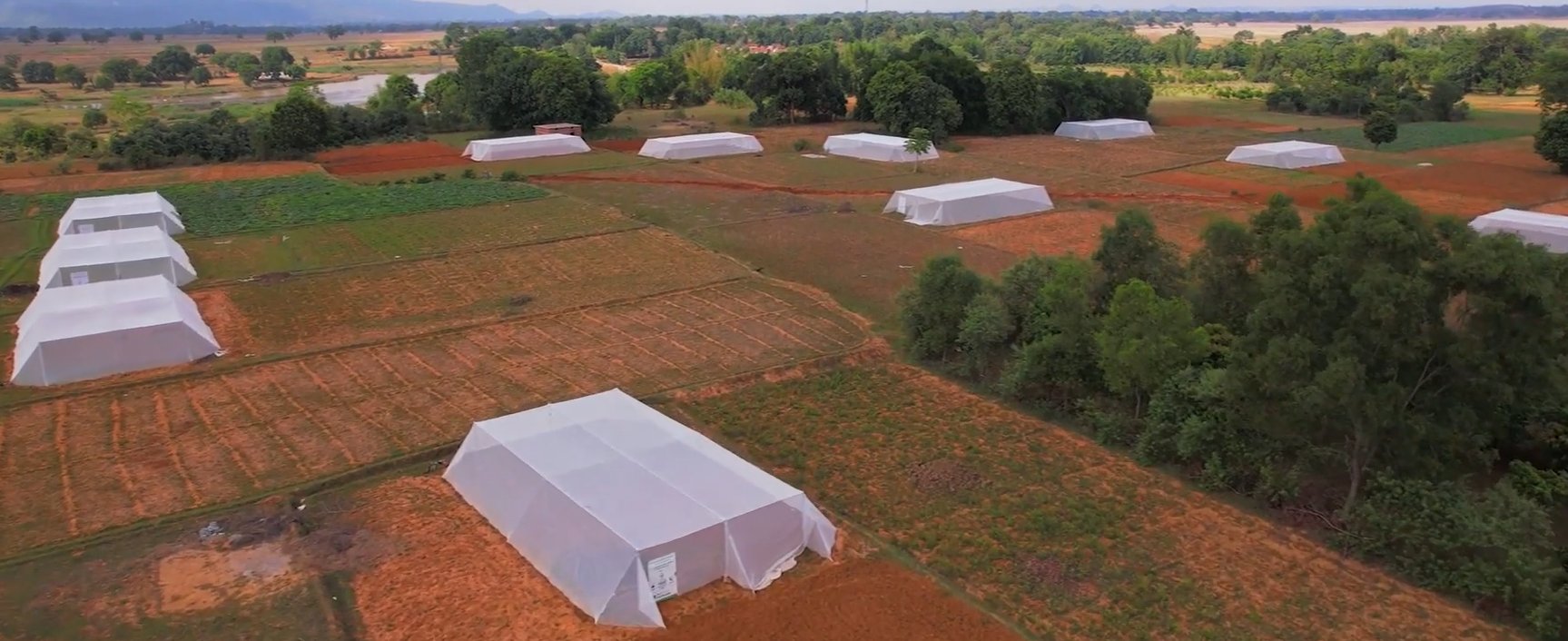 Aerial view of rows of shade net and polyhouse structures across farm plots